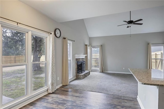 unfurnished living room with lofted ceiling, a fireplace with raised hearth, ceiling fan, dark wood-style flooring, and baseboards