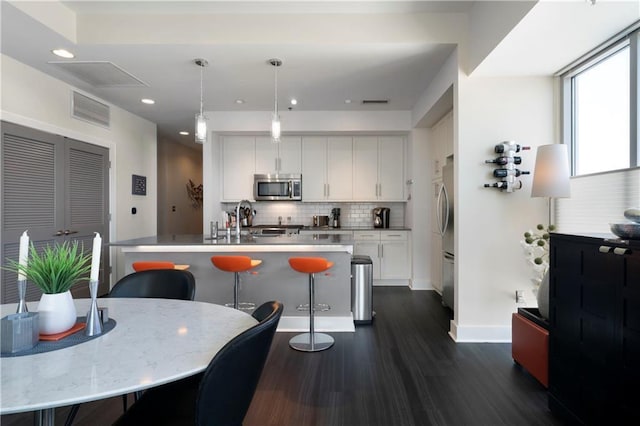 kitchen with white cabinets, appliances with stainless steel finishes, decorative light fixtures, and a center island with sink