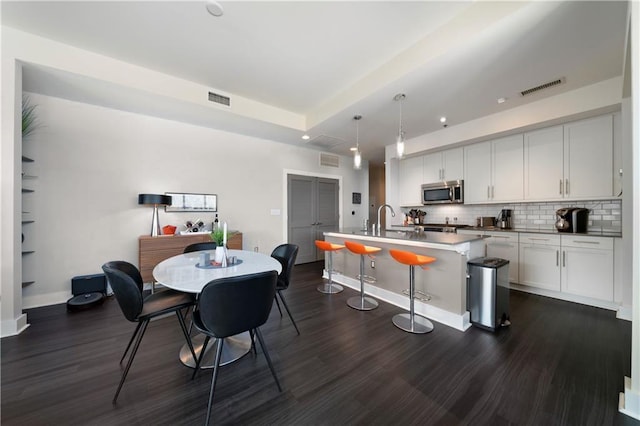 kitchen featuring white cabinets, dark hardwood / wood-style flooring, an island with sink, and decorative light fixtures