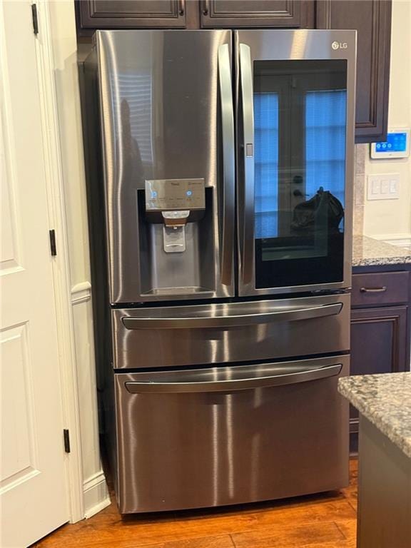 details with hardwood / wood-style flooring, stainless steel refrigerator with ice dispenser, light stone countertops, and dark brown cabinets