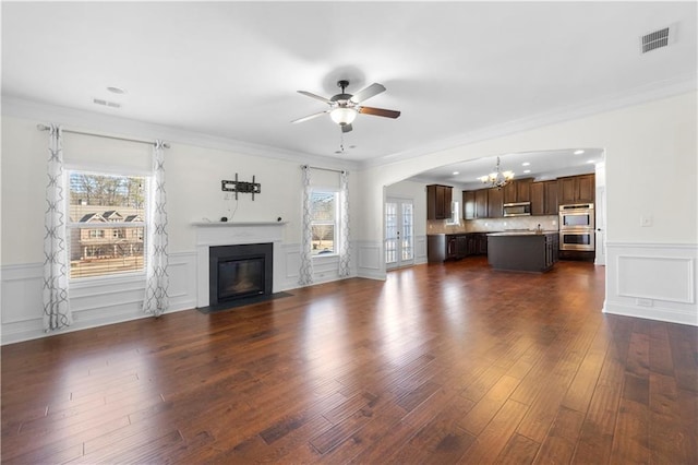 unfurnished living room with ornamental molding, ceiling fan with notable chandelier, and dark hardwood / wood-style flooring