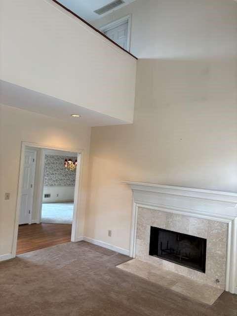 unfurnished living room featuring visible vents, baseboards, carpet floors, a fireplace, and a high ceiling