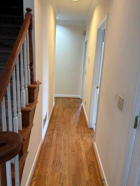 corridor featuring light wood-type flooring, baseboards, ornamental molding, and stairway