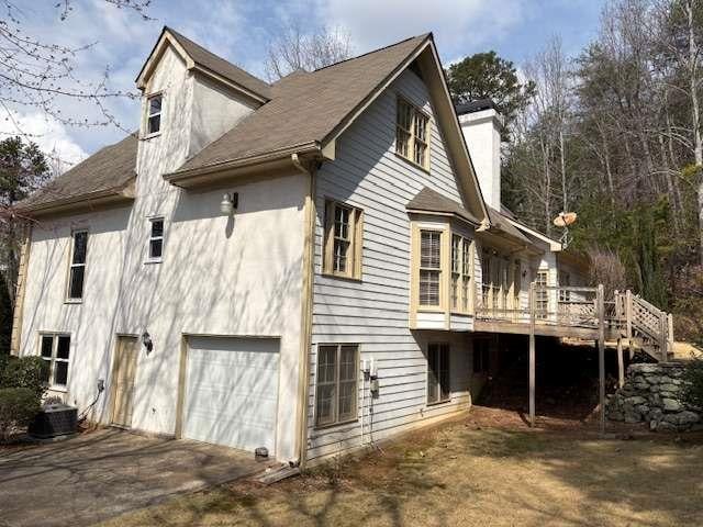 view of home's exterior with stucco siding, a chimney, driveway, a deck, and an attached garage