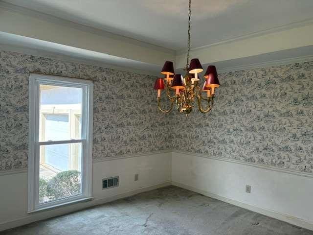 unfurnished dining area with visible vents, wallpapered walls, ornamental molding, wainscoting, and a notable chandelier