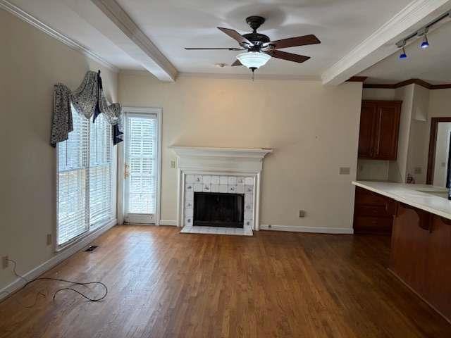 unfurnished living room with beam ceiling, ornamental molding, wood finished floors, baseboards, and ceiling fan