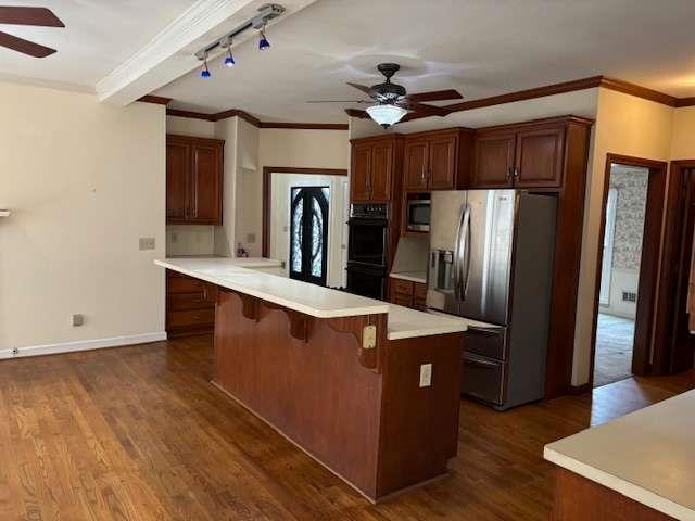 kitchen with dark wood-type flooring, a breakfast bar, appliances with stainless steel finishes, light countertops, and ceiling fan