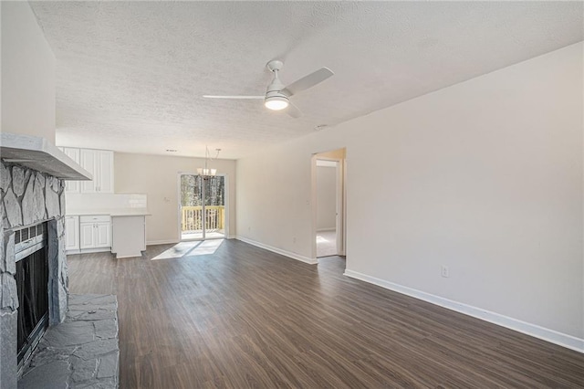 unfurnished living room with a fireplace, a textured ceiling, dark hardwood / wood-style flooring, and ceiling fan with notable chandelier