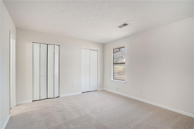 unfurnished bedroom featuring light carpet, a textured ceiling, and two closets