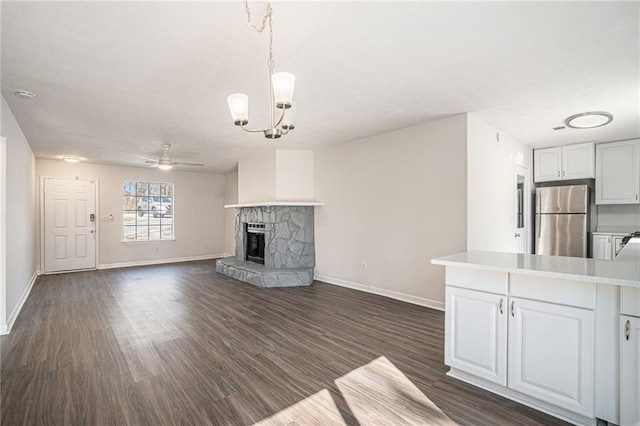 unfurnished living room with dark hardwood / wood-style flooring, ceiling fan with notable chandelier, and a stone fireplace