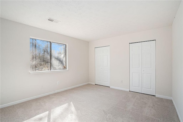 unfurnished bedroom with two closets and light colored carpet