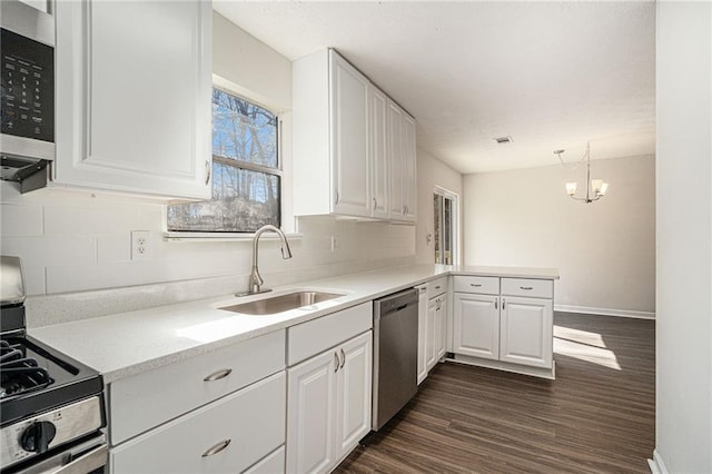 kitchen with sink, dark wood-type flooring, stainless steel appliances, pendant lighting, and white cabinets