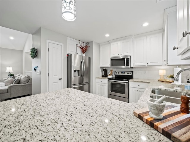 kitchen with appliances with stainless steel finishes, white cabinetry, light stone countertops, and sink