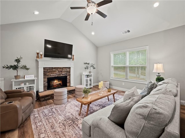 living room with dark hardwood / wood-style flooring, ceiling fan, vaulted ceiling, and a stone fireplace