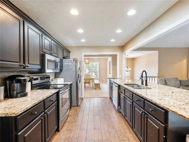 kitchen with stainless steel appliances, a sink, light wood-style floors, light stone counters, and recessed lighting