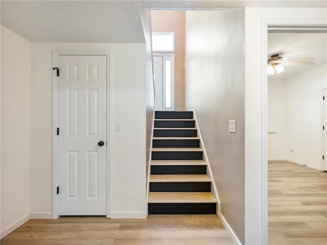 stairs featuring wood finished floors, a ceiling fan, and baseboards