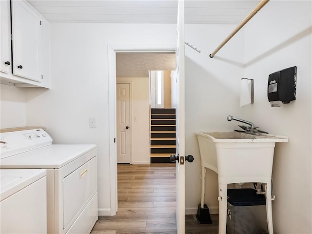 clothes washing area with cabinet space, washing machine and dryer, light wood-style floors, and baseboards