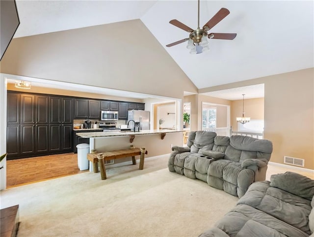 living area featuring high vaulted ceiling, a chandelier, a ceiling fan, light carpet, and baseboards