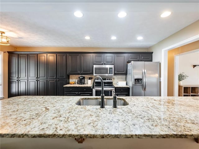 kitchen featuring appliances with stainless steel finishes, a sink, light stone counters, and recessed lighting
