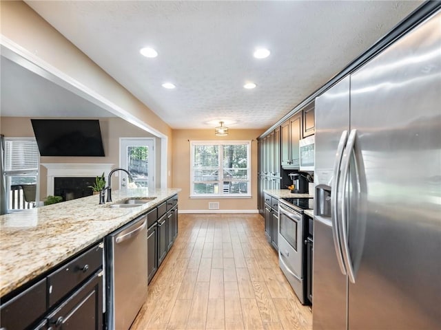 kitchen featuring stainless steel appliances, a sink, recessed lighting, light stone counters, and light wood-type flooring