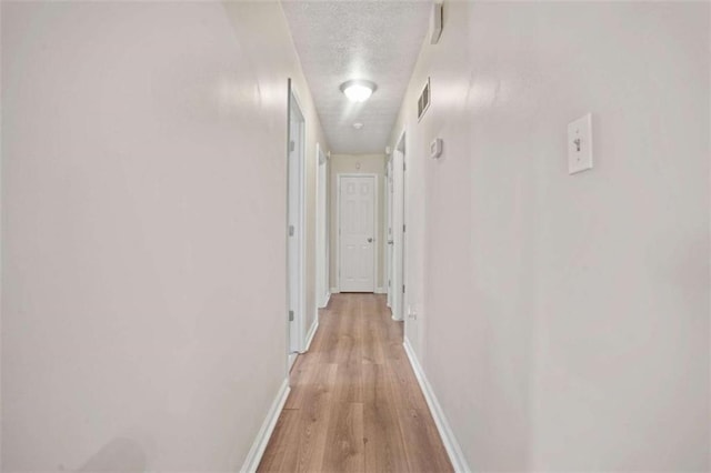 hallway with a textured ceiling and light wood-type flooring