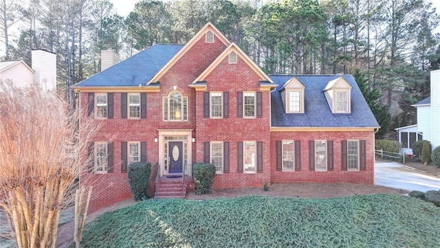 colonial home with brick siding, a chimney, and a front yard