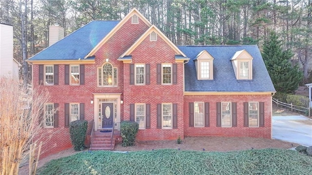 view of front facade with roof with shingles, brick siding, and a chimney