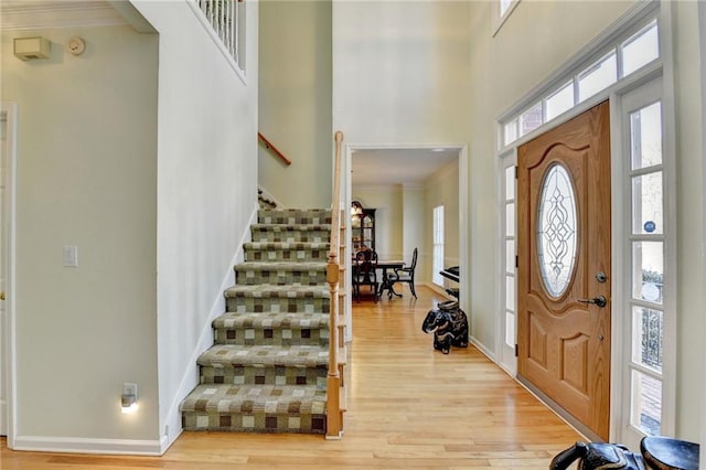 entryway featuring crown molding, light wood-style flooring, a high ceiling, baseboards, and stairs