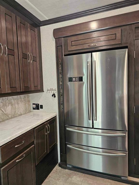 kitchen with decorative backsplash, dark brown cabinets, stainless steel refrigerator, and ornamental molding