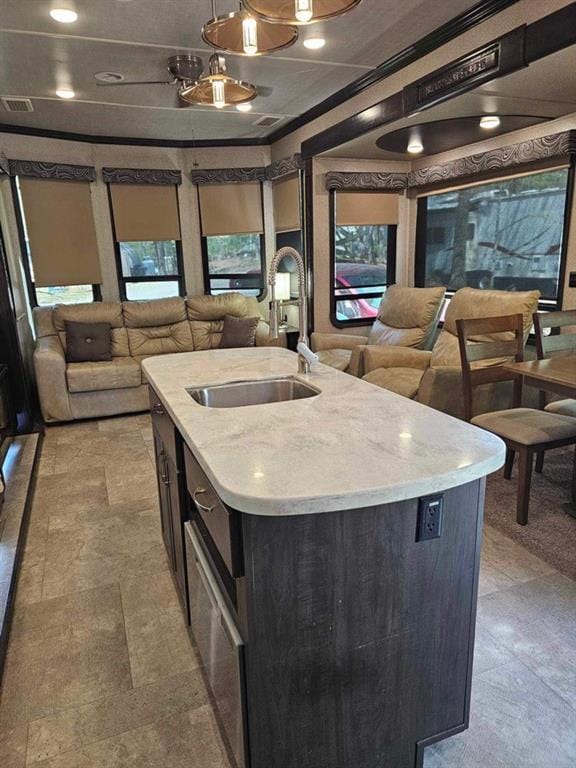 kitchen with ornamental molding, sink, light tile patterned floors, and a kitchen island with sink