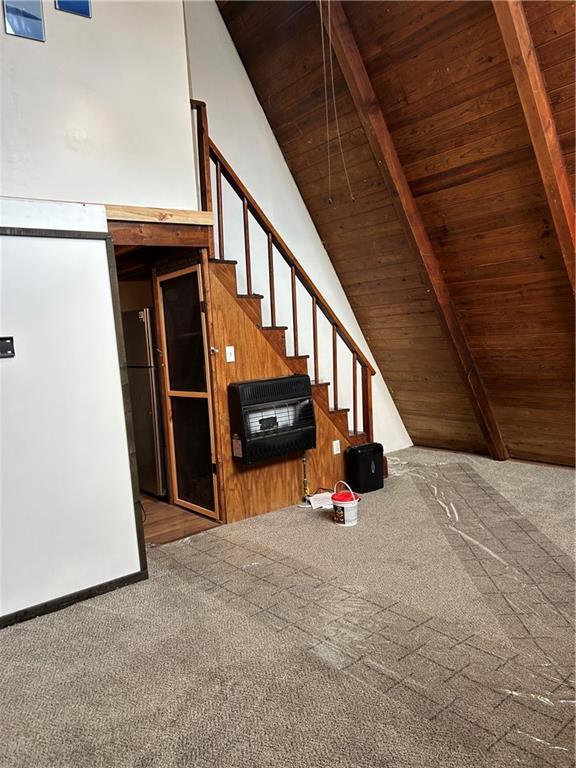 interior space featuring heating unit, wood ceiling, wooden walls, carpet floors, and beamed ceiling