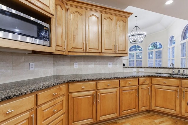 kitchen with stainless steel microwave, sink, hanging light fixtures, a notable chandelier, and dark stone countertops