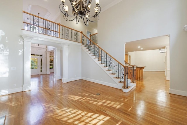 interior space featuring ornate columns, a towering ceiling, a chandelier, and hardwood / wood-style flooring