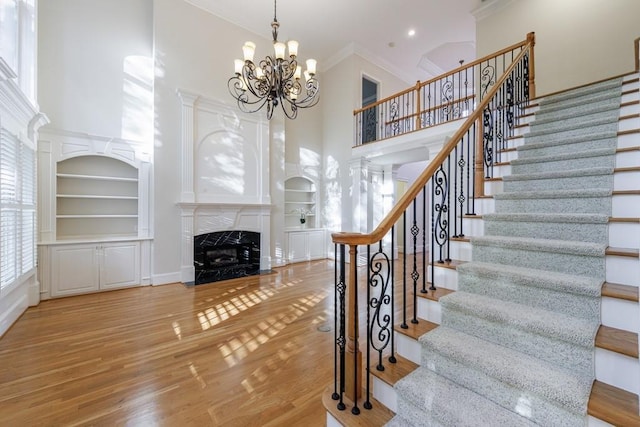 stairs featuring a towering ceiling, crown molding, wood-type flooring, a notable chandelier, and a fireplace