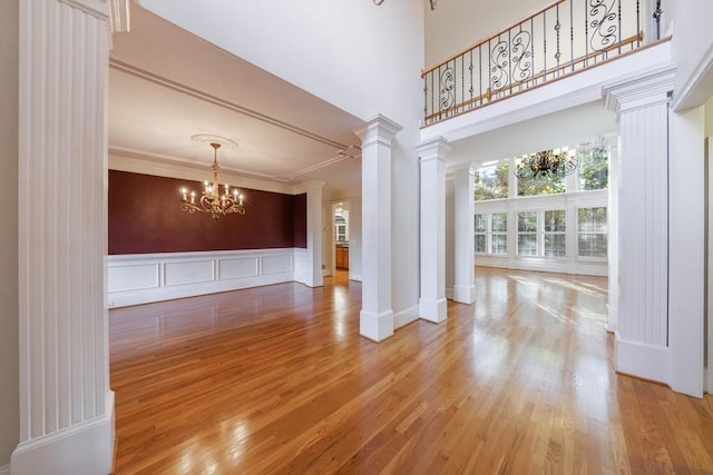 interior space featuring a high ceiling, ornate columns, ornamental molding, wood-type flooring, and a chandelier