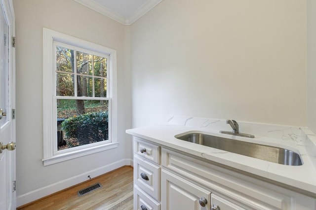 interior space with light stone countertops, ornamental molding, sink, white cabinets, and light hardwood / wood-style floors