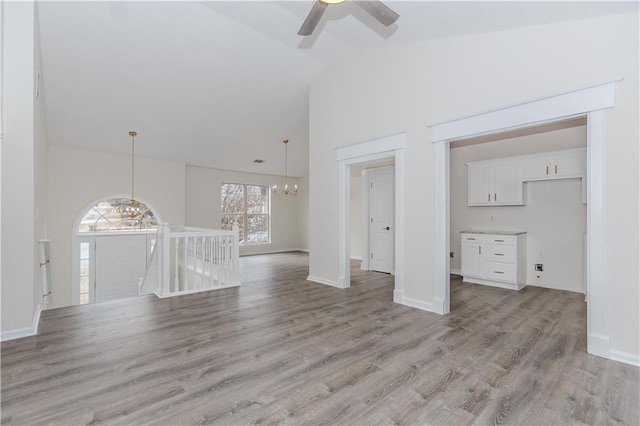 unfurnished living room featuring ceiling fan with notable chandelier, high vaulted ceiling, and light wood-type flooring