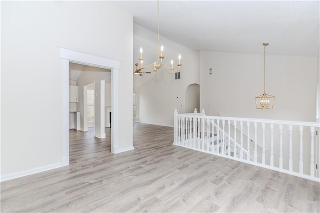 empty room with high vaulted ceiling, a chandelier, and light wood-type flooring