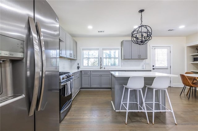 kitchen with a sink, range with gas stovetop, light countertops, gray cabinets, and stainless steel fridge