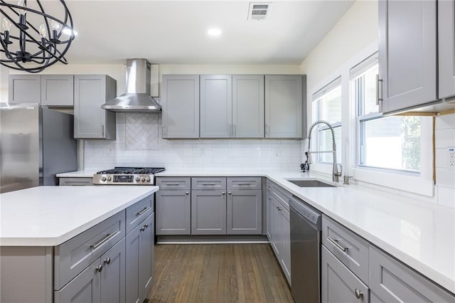 kitchen with a sink, stainless steel appliances, wall chimney range hood, and gray cabinets