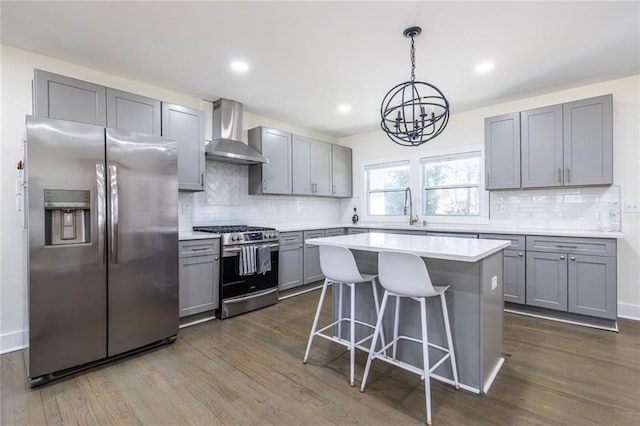 kitchen featuring a breakfast bar area, gray cabinetry, stainless steel appliances, light countertops, and wall chimney exhaust hood