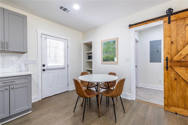 dining room featuring a barn door, electric panel, visible vents, and wood finished floors