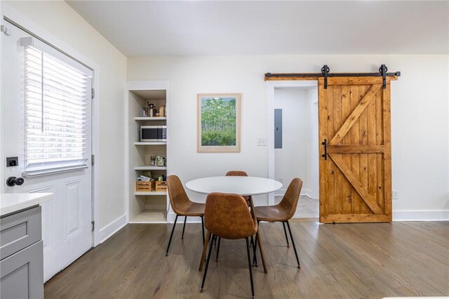 dining room with a barn door, dark wood-type flooring, electric panel, and a healthy amount of sunlight