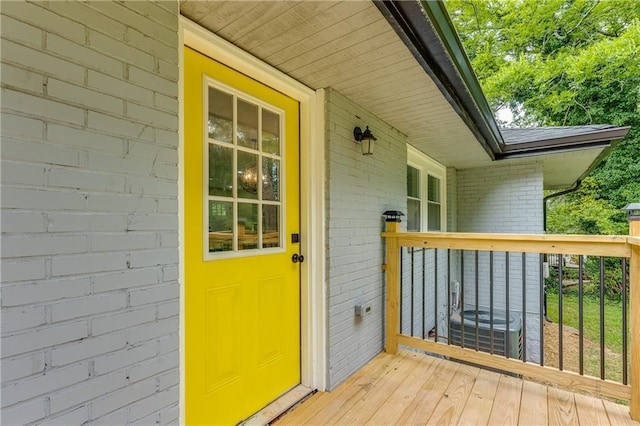 doorway to property featuring roof with shingles, central AC unit, and brick siding