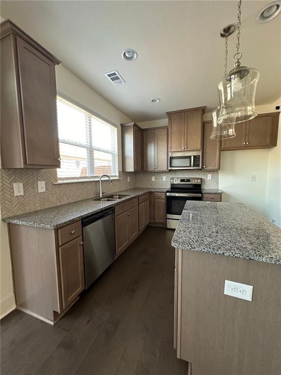 kitchen with light stone countertops, appliances with stainless steel finishes, sink, dark hardwood / wood-style floors, and hanging light fixtures