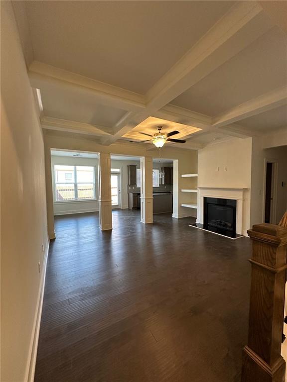 unfurnished living room featuring ceiling fan, coffered ceiling, dark hardwood / wood-style flooring, beamed ceiling, and ornamental molding