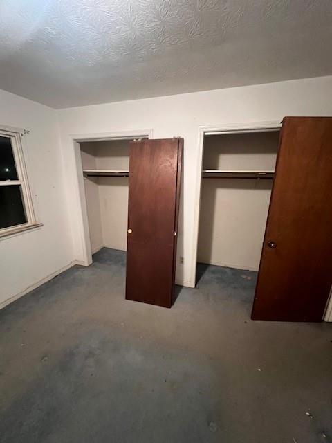 unfurnished bedroom with a textured ceiling and multiple closets