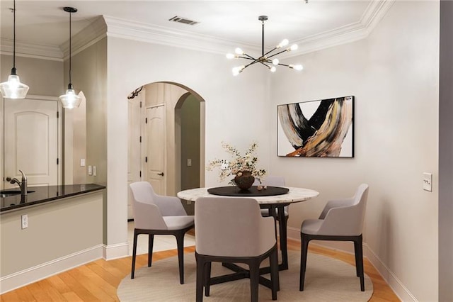 dining area with crown molding, sink, light wood-type flooring, and a notable chandelier