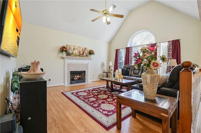 living room with hardwood / wood-style floors, ceiling fan, lofted ceiling, and a tiled fireplace