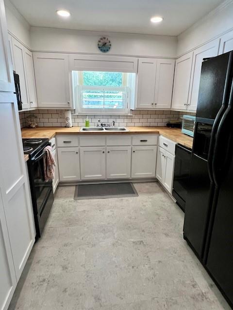 kitchen with wooden counters, a sink, decorative backsplash, black appliances, and white cabinets